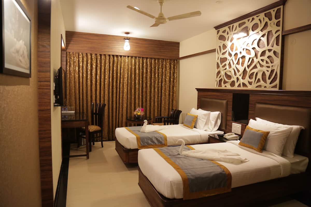 A hotel room with two beds, a desk with a chair, a ceiling fan, and a decorative wall panel.