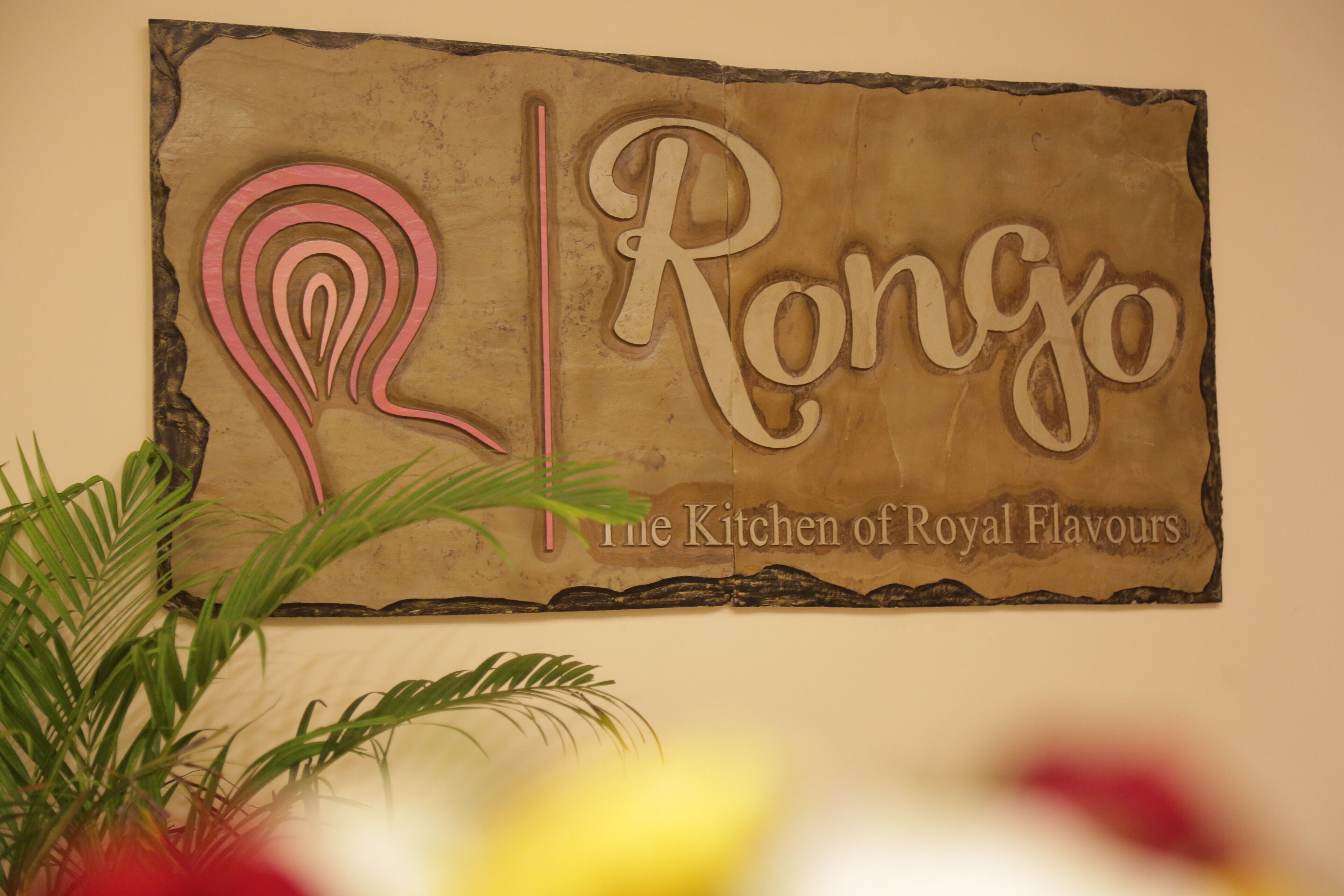 A sign with the text "Rongo The Kitchen of Royal Flavours" on a textured wall.