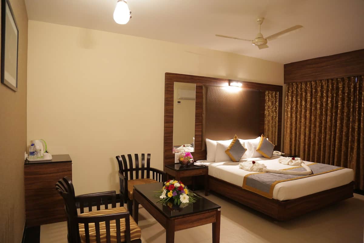 A hotel room with a bed, a desk, a chair, a mirror, and a ceiling fan.