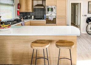 A modern kitchen with wooden cabinets, a white countertop, and two wooden stools. - 3 bedroom accommodation in Carnforth (Carnforth)