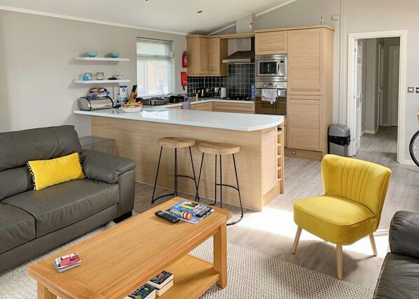 A modern kitchen with a central island, bar stools, and a dining area with a sofa and coffee table.