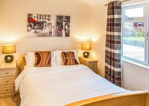 A hotel room with a bed, two bedside tables with lamps, a wall-mounted picture, and a window with curtains. - 3 bedroom accommodation in Carnforth (Carnforth)