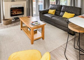 A living room with a sofa, a coffee table, a fireplace, and a view through the window. - 3 bedroom accommodation in Carnforth (Carnforth)