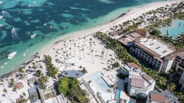 Ein Luftbild eines Küstenresorts mit Strand, Schwimmbad und mehreren Booten im Wasser.
