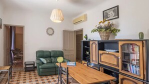 A living room with a green sofa, a wooden dining table, a chandelier, a bookshelf, and a cactus. - Gîte piscine** Chez Mémé de la Maréchale (Orgnac-l'Aven)