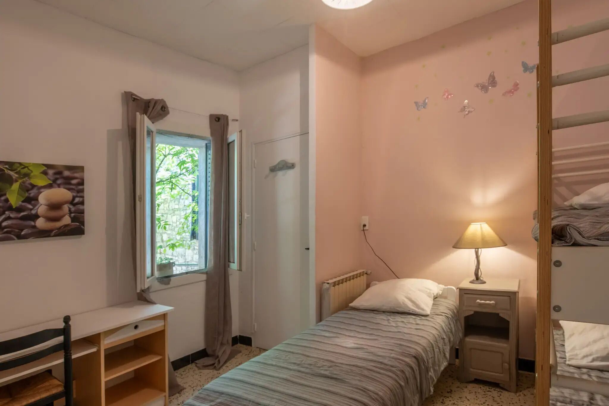 Un dormitorio con una cama individual, un escritorio, un radiador, una mesita de noche con lámpara y una ventana con cortinas.