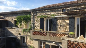A stone building with a tiled roof, multiple windows, and a balcony with plants. - Gîte piscine** Chez Mémé de la Maréchale (Orgnac-l'Aven)