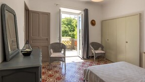 A room with a bed, two chairs, a wardrobe, a mirror, and a door leading to an outdoor area. - Gîte piscine** Chez Mémé de la Maréchale (Orgnac-l'Aven)