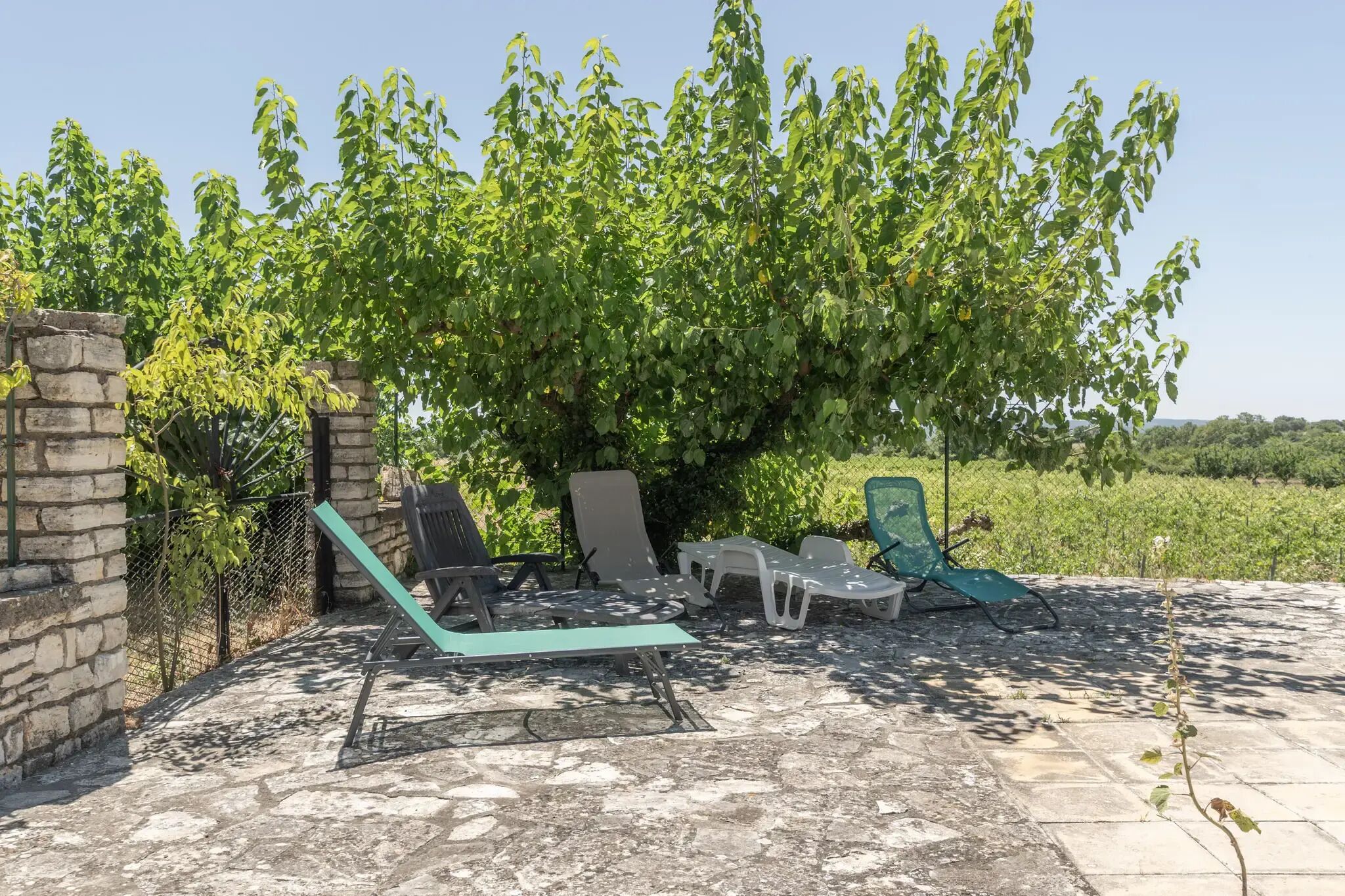 A patio area with stone flooring, a stone wall, and a row of lounge chairs and a table.