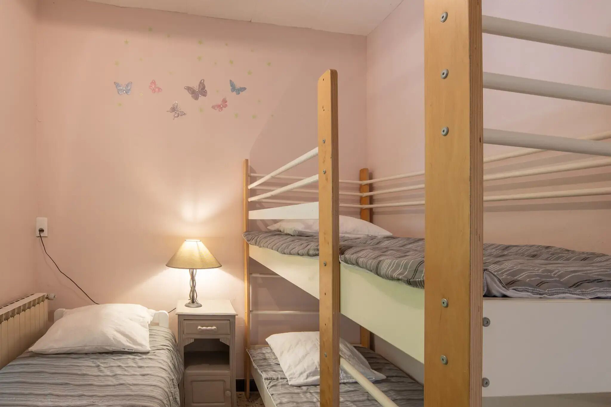 A bunk bed room with a nightstand and lamp, a wall with butterfly decals, and a power outlet.