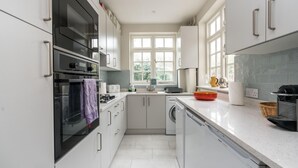 A modern kitchen with white cabinetry, a built-in oven, a dishwasher, and a window providing natural light. - Charming 2BD Garden House - Hammersmith (London)