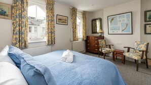 A hotel room with a bed, a dresser, two chairs, a mirror, and framed pictures on the wall. - Charming 2BD Garden House - Hammersmith (London)