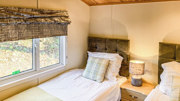A bedroom with a bed, a nightstand, a lamp, and a window with a view of greenery. - Borwick Heights 10 is ideal for a relaxing getaway. (Carnforth)