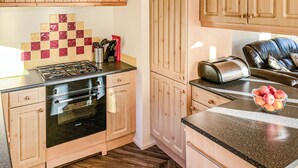 A kitchen with wooden cabinets, a gas stove, an oven, a toaster, and a bowl of fruit on the counter. - Borwick Heights 10 is ideal for a relaxing getaway. (Carnforth)