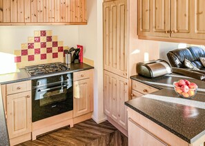 A kitchen with wooden cabinets, a gas stove, an oven, a toaster, and a bowl of fruit on the counter. - Borwick Heights 10 is ideal for a relaxing getaway. (Carnforth)