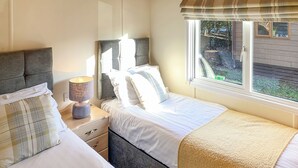 A bedroom with two beds, a nightstand with a lamp, and a window with a view of the outside. - Borwick Heights 10 is ideal for a relaxing getaway. (Carnforth)