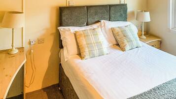 A neatly made bed with a grey headboard, two bedside lamps, and a bedside table with a lamp.