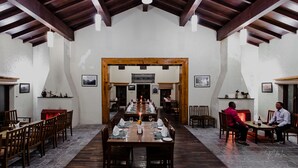 A dining area with a long table set for a meal, wooden beams on the ceiling, and a fireplace in the background.