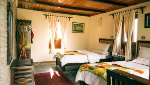 A room with two beds, a wooden ceiling, a red rug, and a wooden bench.