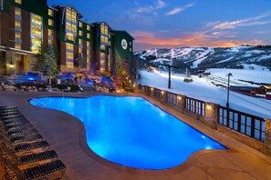 Ein Hotel mit Swimmingpool, Sitzgelegenheiten im Freien und Blick auf einen verschneiten Berg.