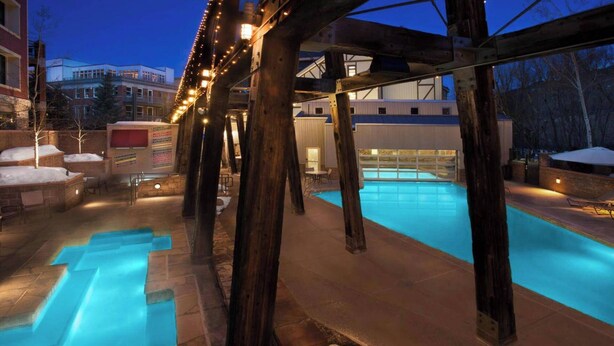 A swimming pool with a wooden deck and stone steps, surrounded by a covered area with string lights.