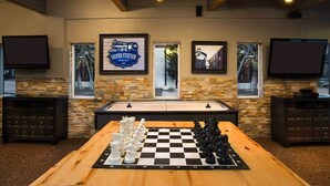 A room with a wooden table set for a game of chess, stone walls, and framed pictures on the wall.