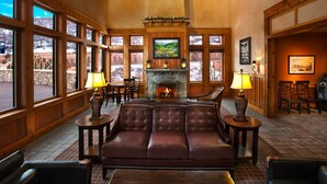 A cozy lobby with a fireplace, leather seating, and large windows offering views of the outdoors.