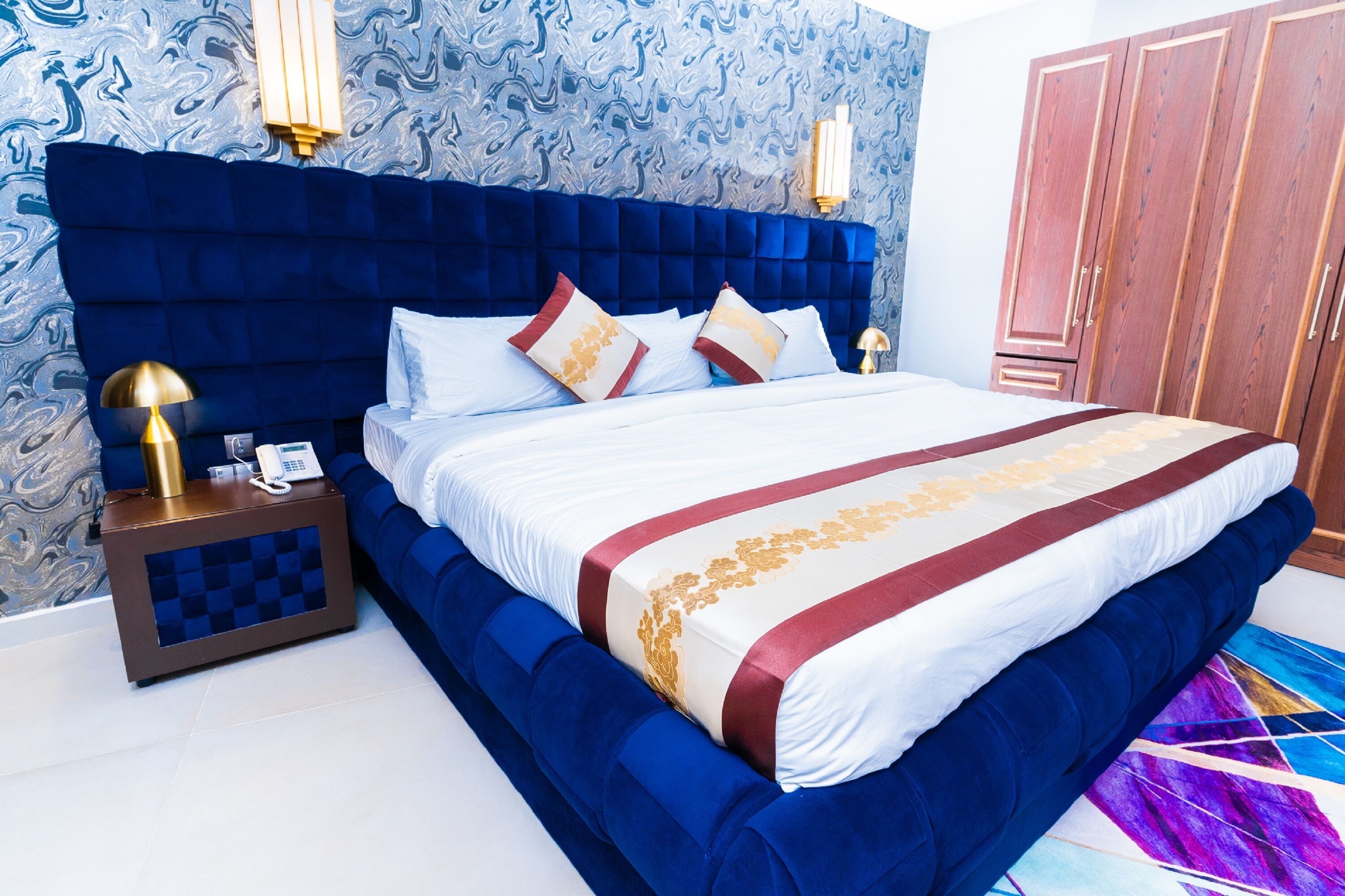 A bedroom with a large bed, a nightstand with a lamp, and a wardrobe.