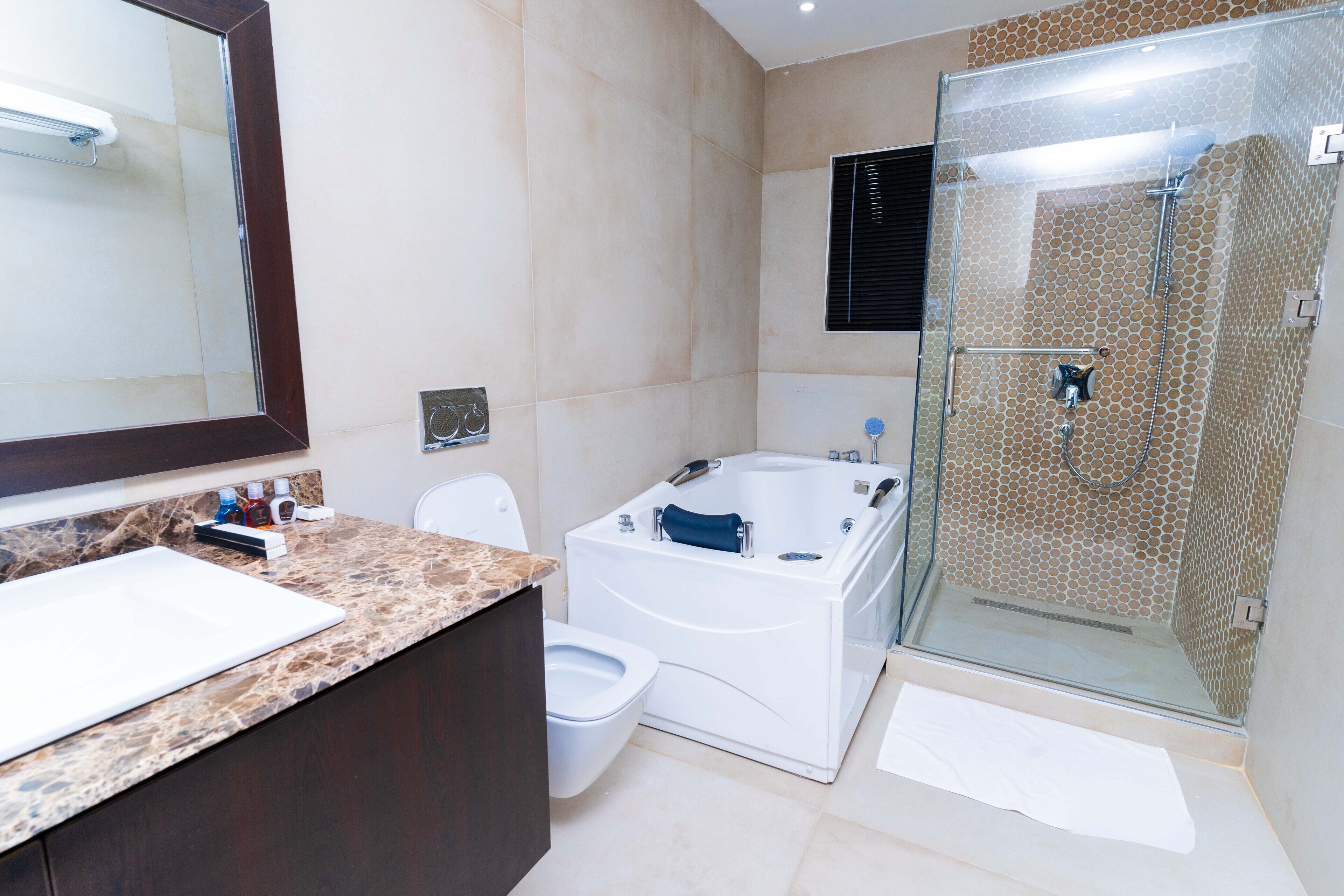 Een moderne badkamer met een marmeren aanrechtblad, een witte badkuip, een douche met glazen wanden en een grote spiegel.
