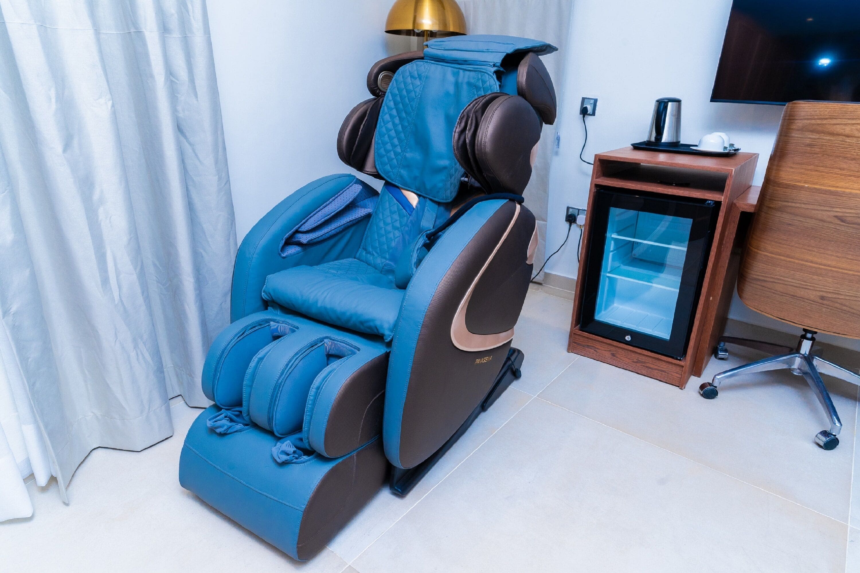 A massage chair with a control panel, a desk, and a television in a room.