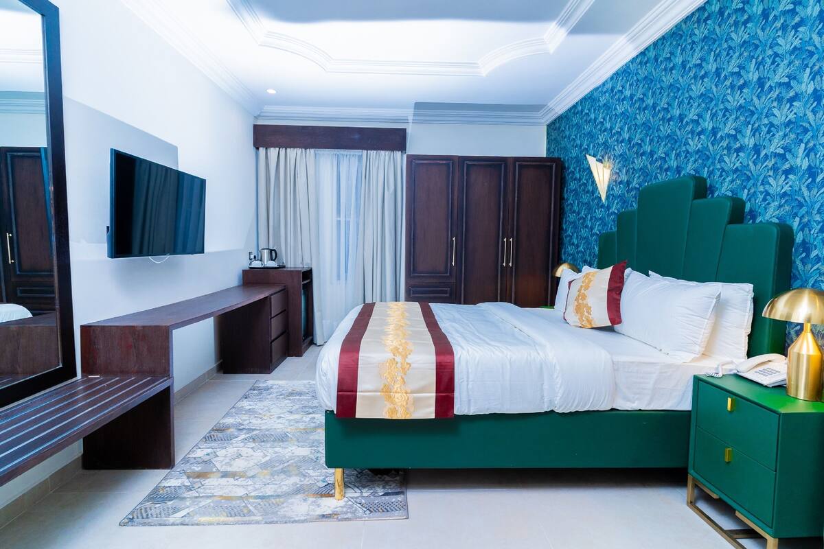 A modern bedroom with a green bed, a flat-screen TV, a desk, and a green nightstand.