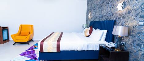 A modern bedroom with a blue bed, a yellow armchair, and a patterned wallpaper.