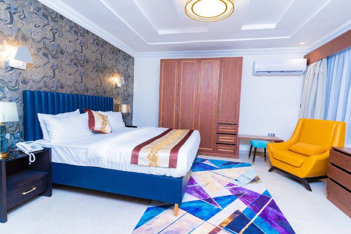 A hotel room with a bed, nightstand, chair, wardrobe, and a desk.