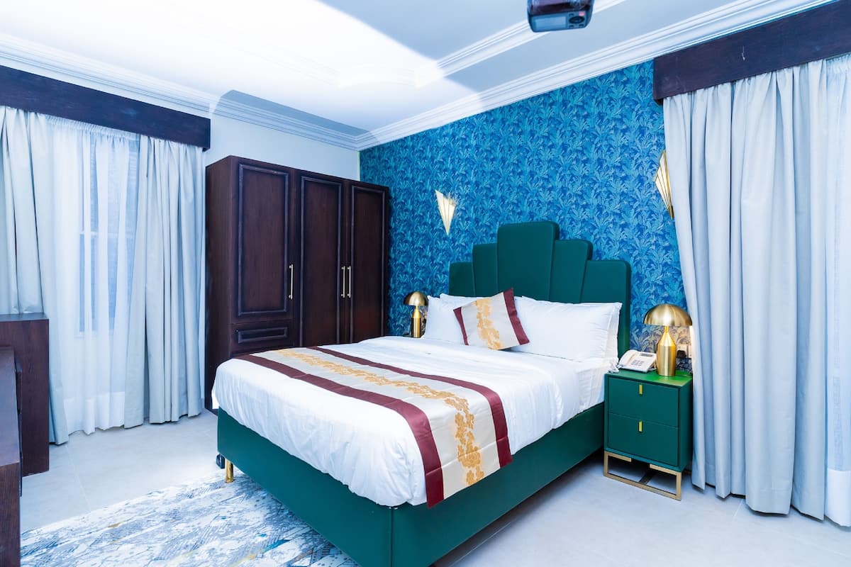 A bedroom with a large bed, a nightstand, a wardrobe, and a blue patterned wall.