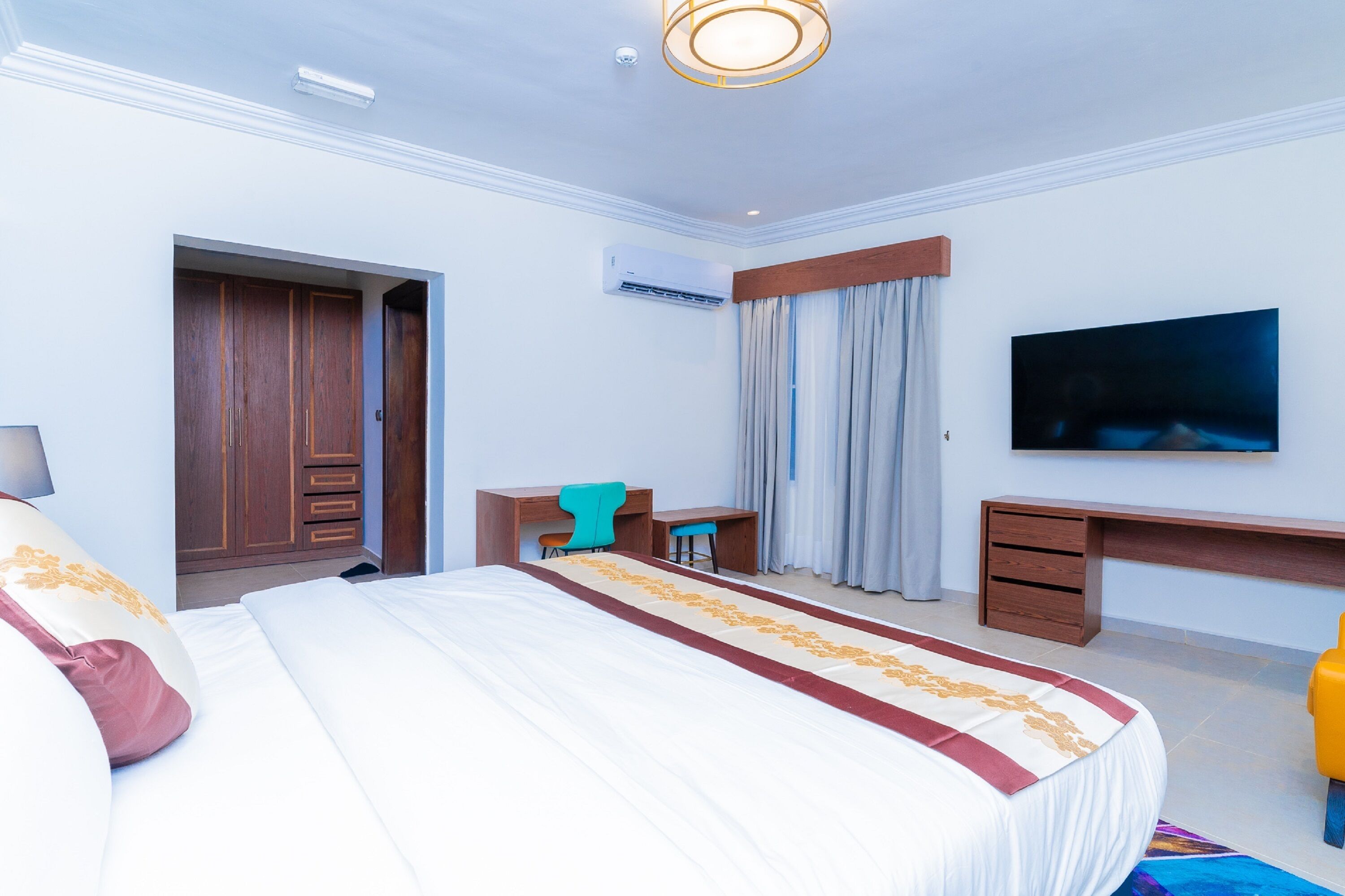 A hotel room with a large bed, a desk, a chair, a TV, and a wardrobe.
