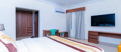 A hotel room with a large bed, a desk, a chair, a TV, and a wardrobe.
