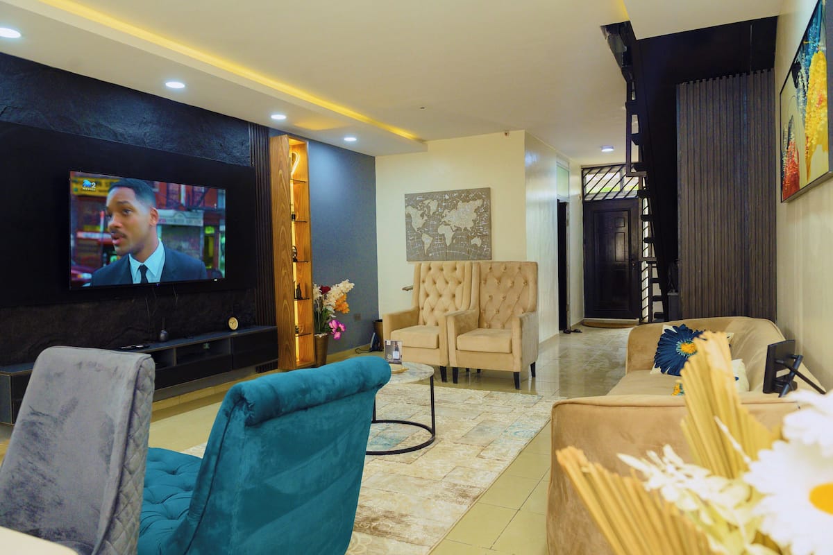 A modern living room with a flat-screen TV, comfortable seating, a world map artwork, and a staircase.