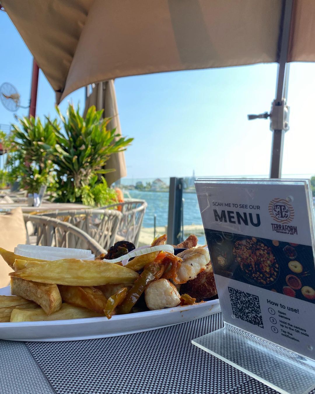 A meal of fries and fish on a table with a menu stand displaying a QR code for a digital menu.