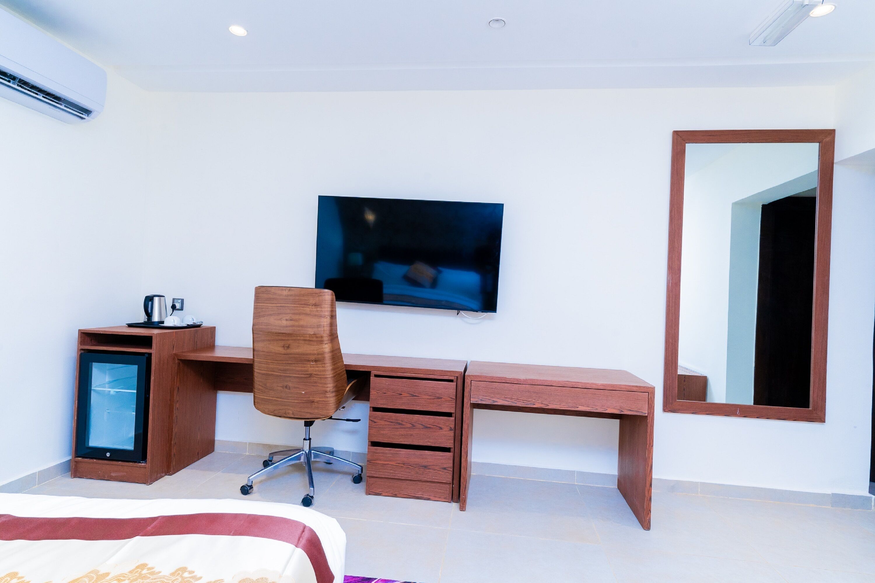 Une chambre d’hôtel moderne, dotée d’un bureau en bois, d’un téléviseur fixé au mur, d’un petit réfrigérateur et d’un grand miroir.