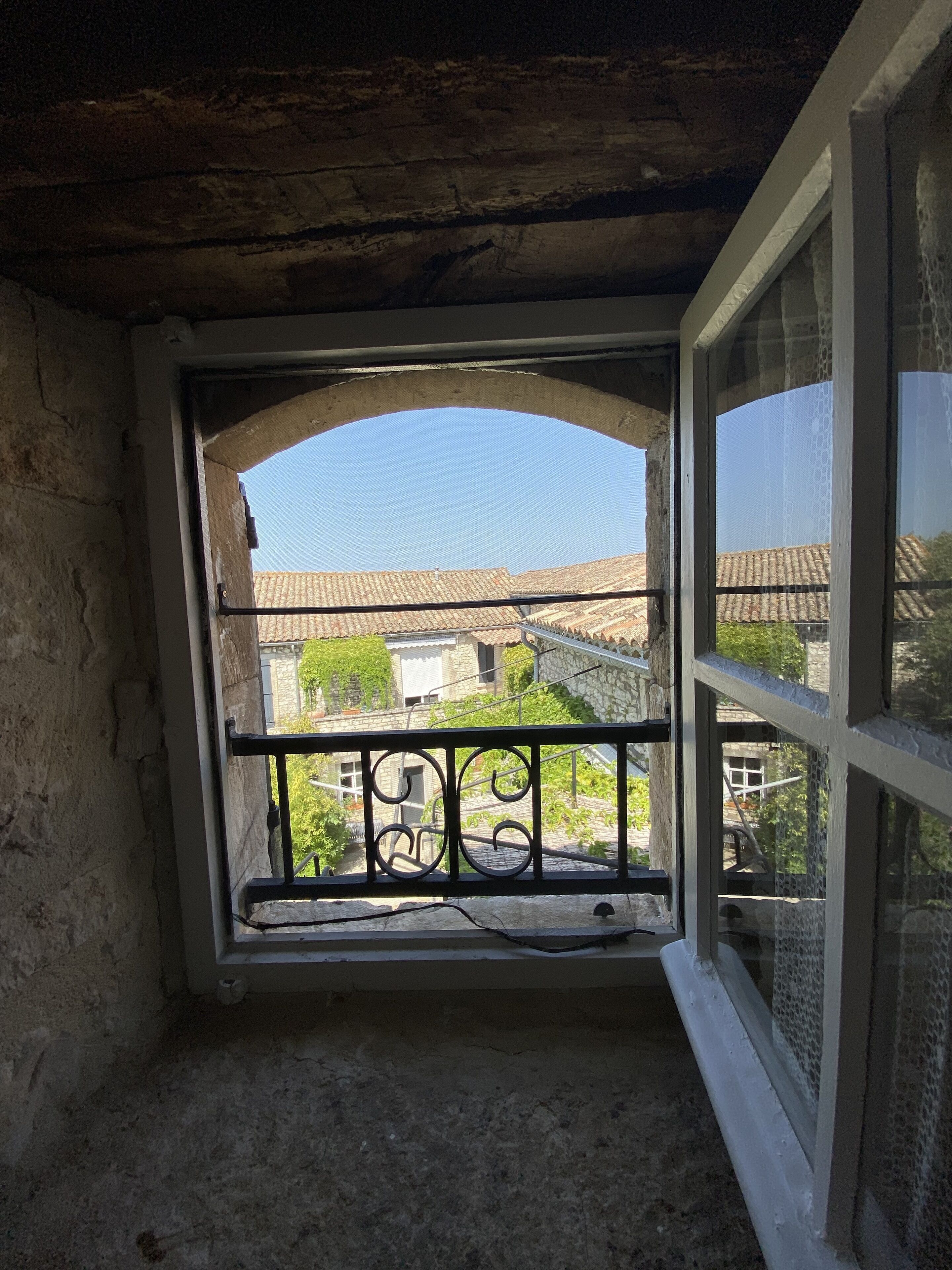 Ein Zimmer mit Fenster und Blick auf einen Innenhof mit Gebäuden und Grünflächen.