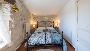 A bedroom with a stone wall, a bed with a metal frame, two bedside lamps, and a radiator.