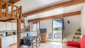 A spacious living area with a red sofa, a dining table with chairs, a kitchen area with white cabinets, and a balcony with a view.
