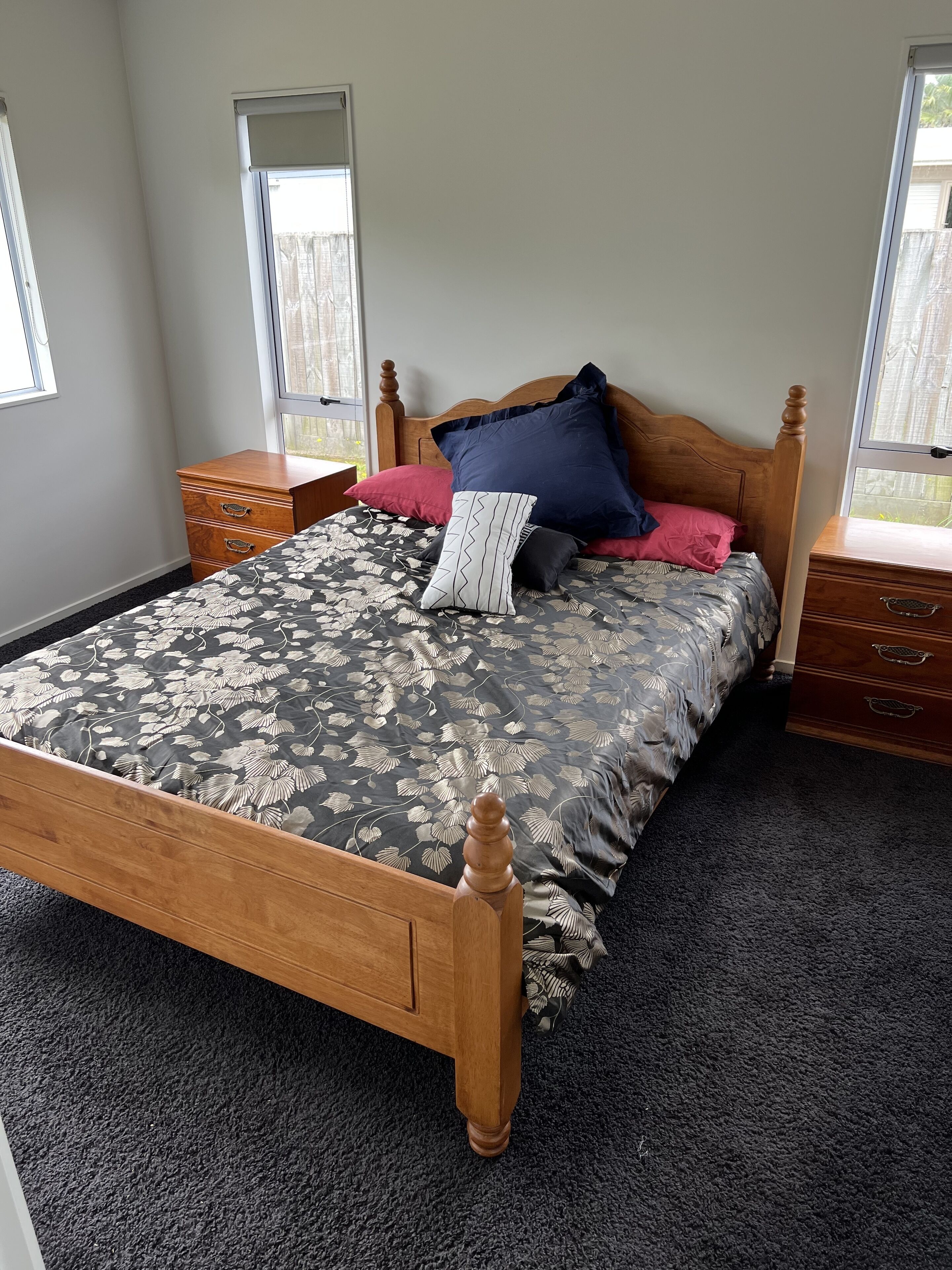 Une chambre à coucher avec un lit en bois, une table de chevet, une commode et deux fenêtres.