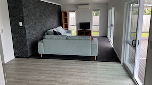 A modern living room with a grey sofa, a flat-screen TV, and a dark patterned wall.