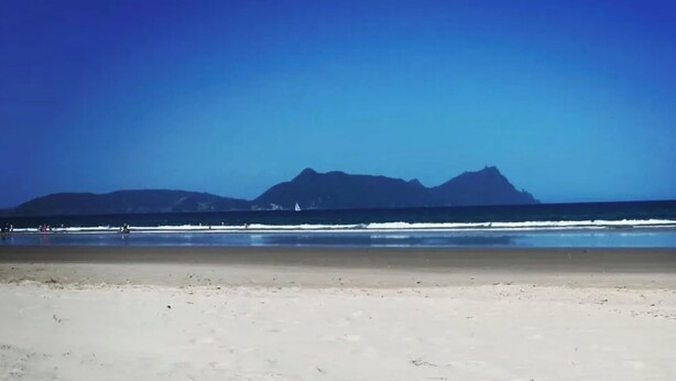 A beach with a clear view of distant mountains under a blue sky.