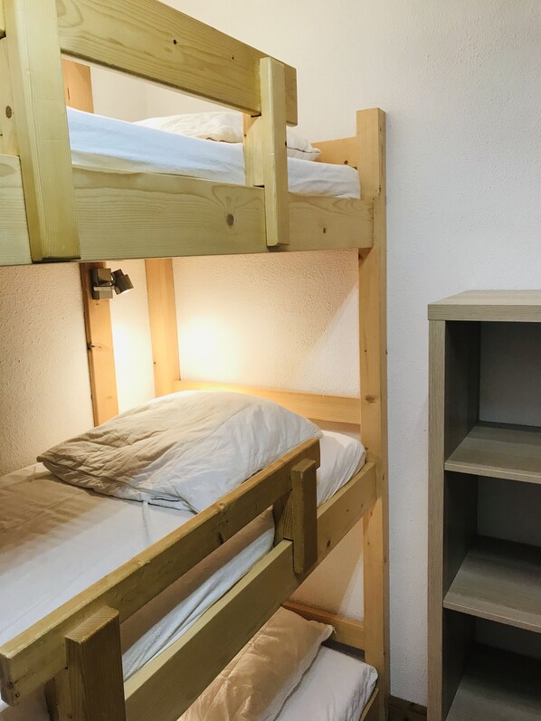 Un letto a castello con struttura in legno e biancheria bianca. A destra del letto, un mobiletto contenitore.