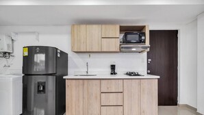 Una cucina compatta con frigorifero, microonde, macchina del caffè e lavello.