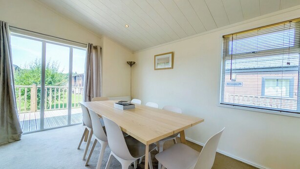 A room with a large table and four chairs, a window with blinds, a picture on the wall, and a view of greenery outside.