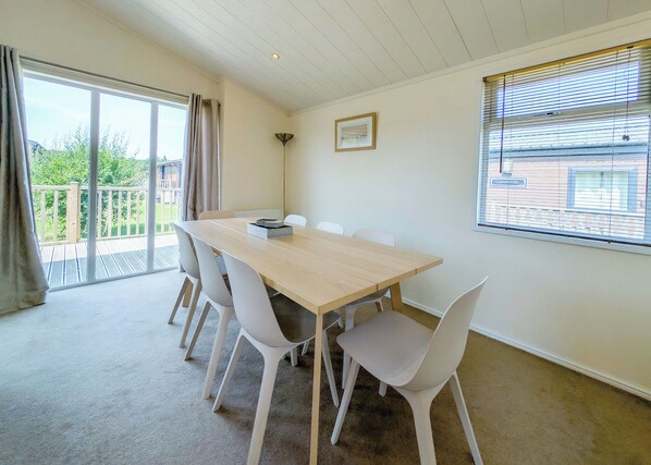 A room with a large table and four chairs, a window with blinds, a picture on the wall, and a view of greenery outside.