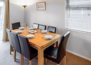 Uma sala de jantar com uma mesa de madeira posta para seis pessoas, rodeada por cadeiras pretas.